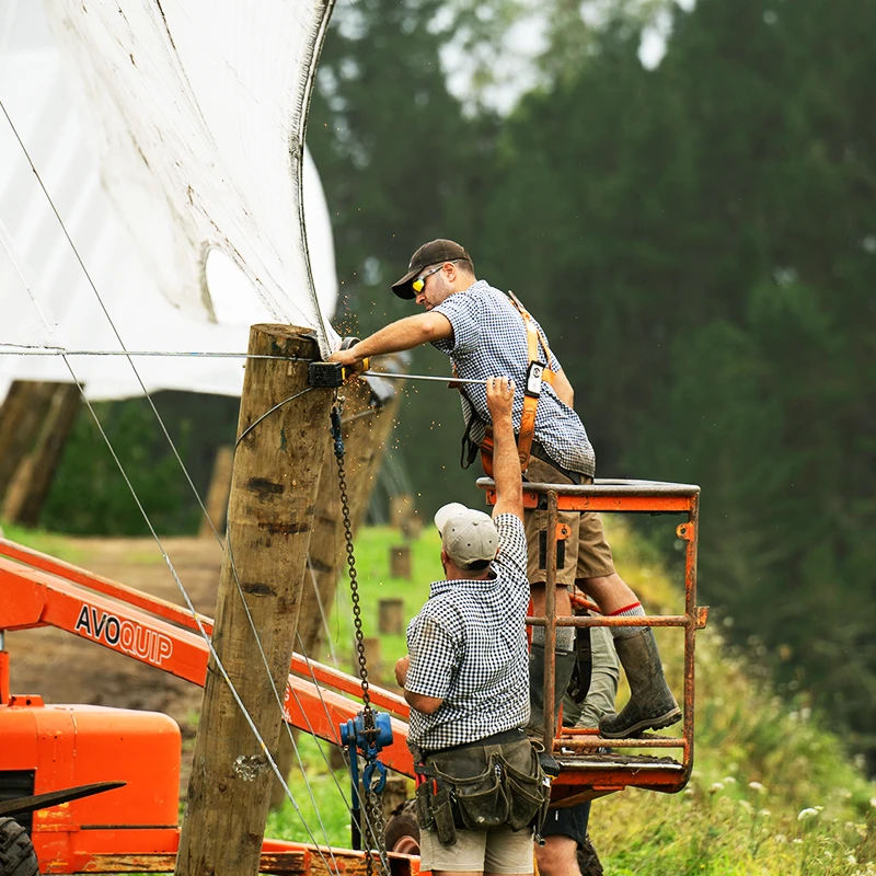 Two men working to secure vertical shelter. A man is positioned on a travel lift and is grinding steel.