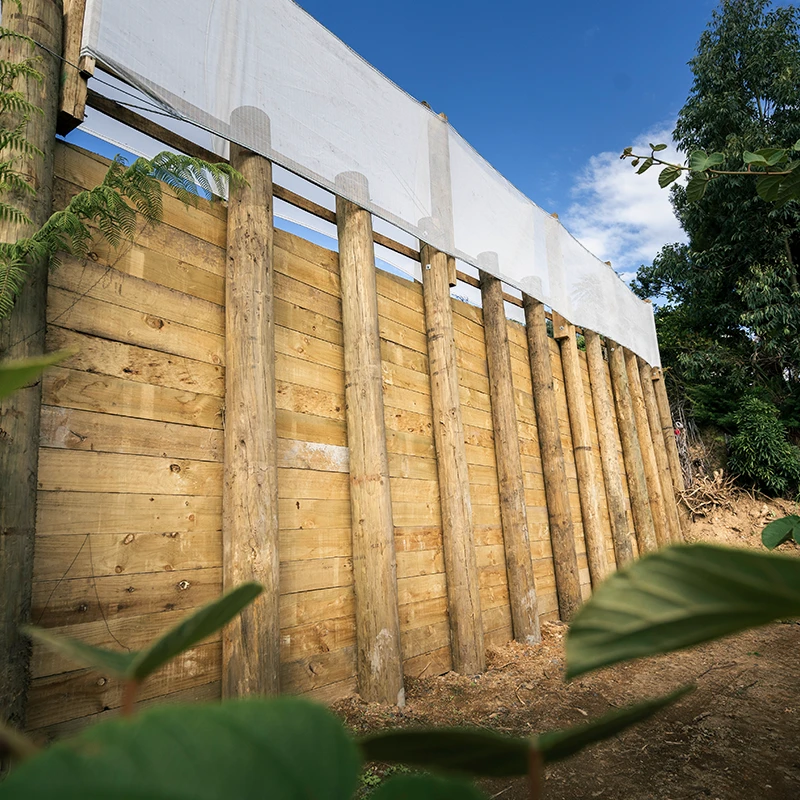 High vertical timber retaining wall with white vertical shelter installed on top, providing both retaining of earth and wind shelter for surrounding crop.